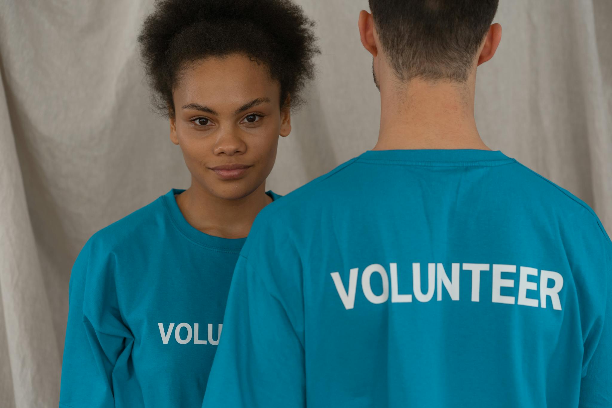 Two volunteers in blue shirts, one smiling and facing camera, promoting support and teamwork.